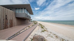 Un edificio moderno con fachada de madera y un paseo marítimo que conduce a una playa.