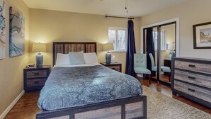 Un dormitorio con cama, mesitas de noche, cómoda, silla, ventilador de techo y un espejo grande.