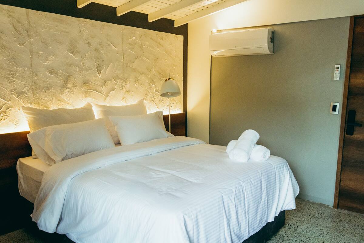 A hotel room with a large bed, a wall-mounted air conditioner, and a door with a handle.