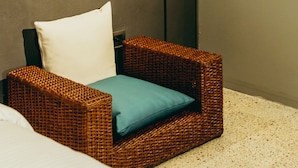 A wicker chair with a white pillow and a teal cushion, positioned next to a tall floor lamp against a plain wall. - I Believe All Suite  (Medellín)