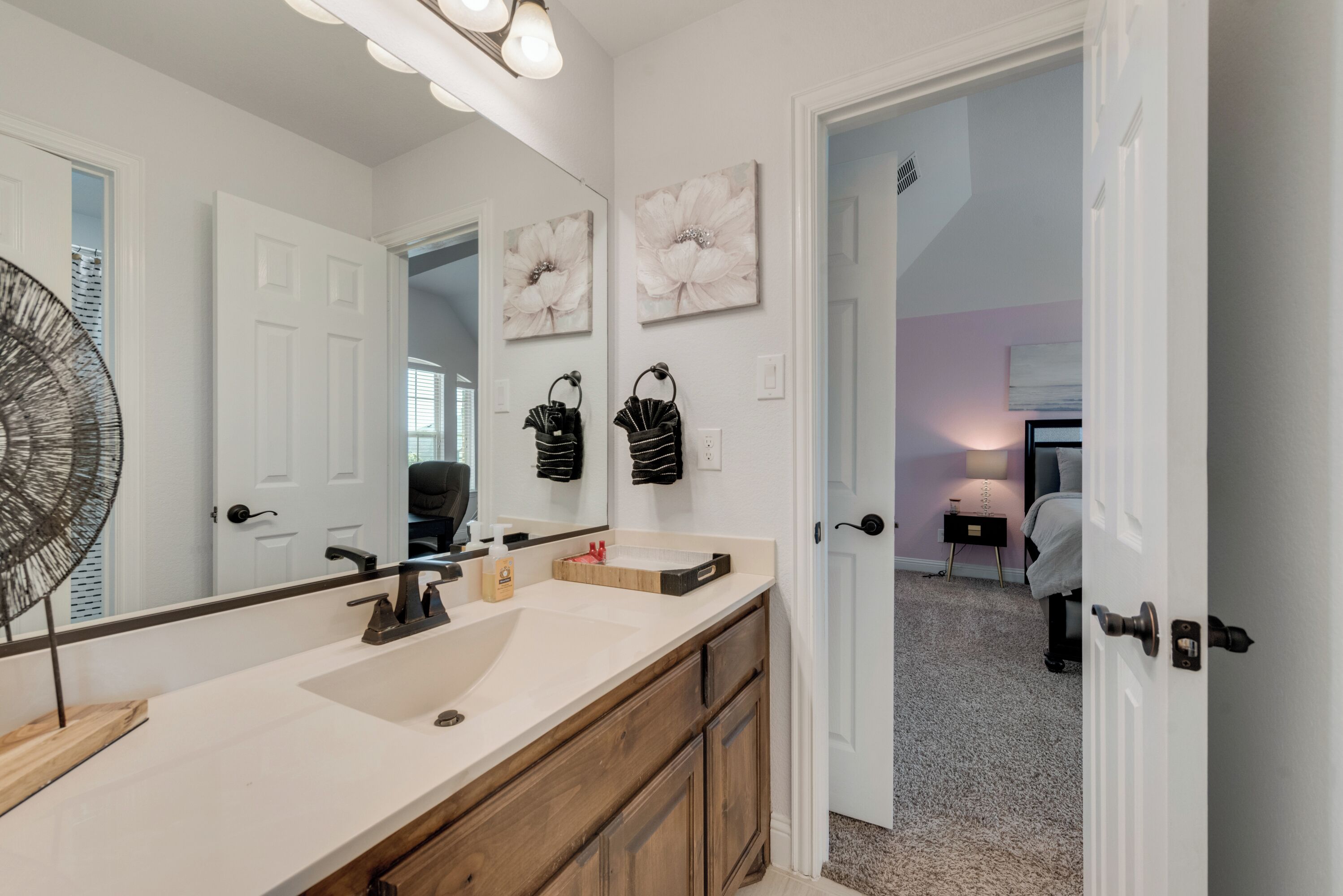 A bathroom with a large mirror, two sinks, wooden cabinets, and a fan.