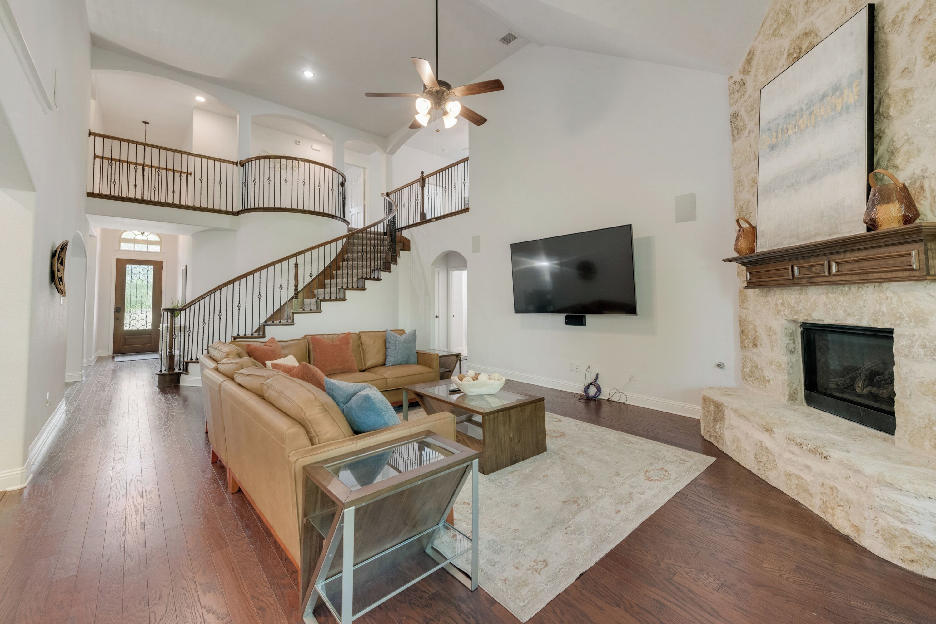 A spacious living room with a curved staircase, a flat-screen TV, and a fireplace.