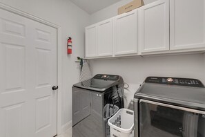A laundry room with two washing machines, a dryer, a fire extinguisher, and a white door. - Gp12 - Luxury 5BD/4BA Mira Lagos home in G Prairie (Grand Prairie)