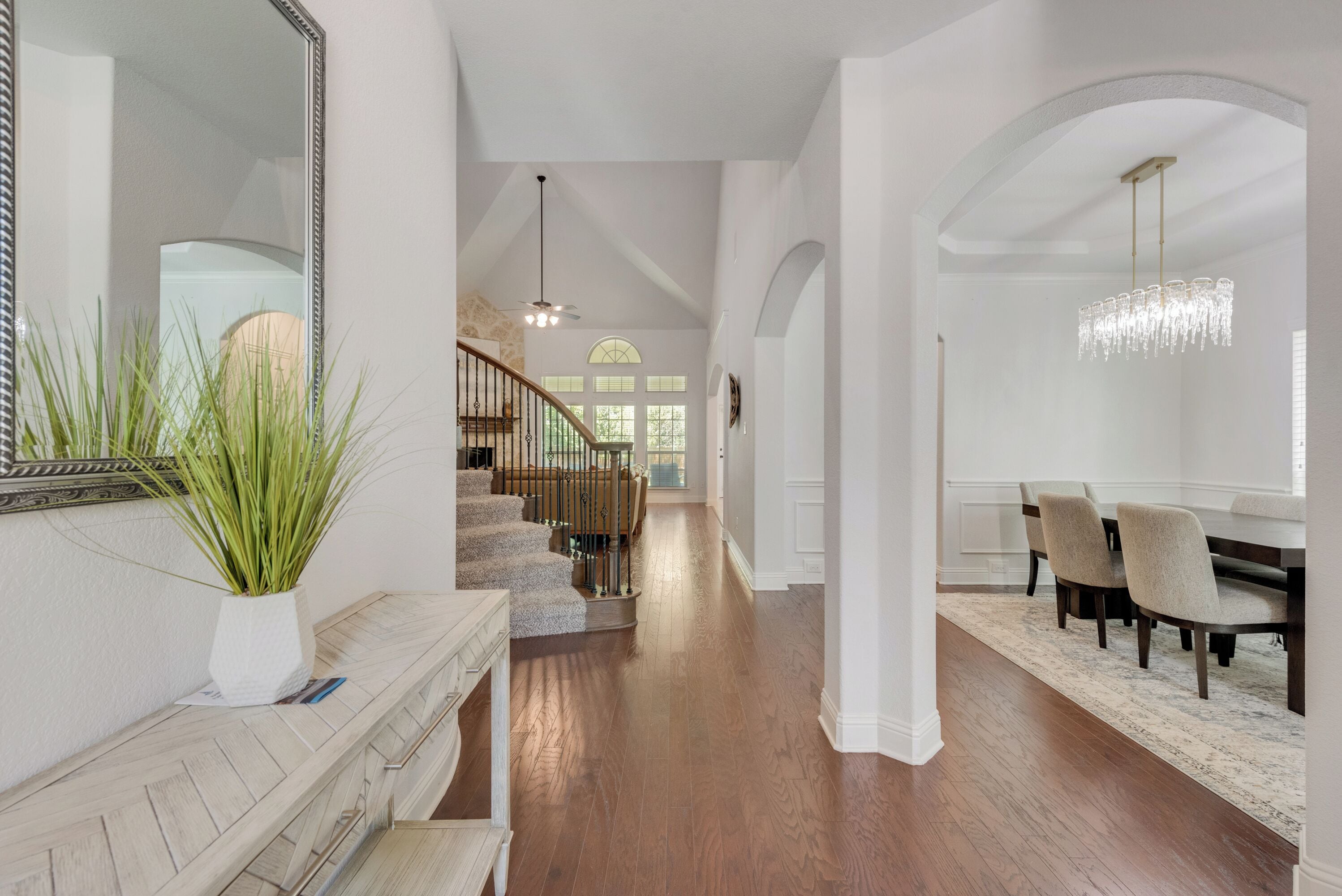 A spacious hallway with a staircase leading to a dining area, featuring a chandelier and a large mirror.