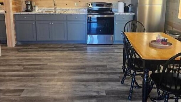 Un intérieur en bois avec un espace cuisine comprenant des armoires grises, un réfrigérateur en acier inoxydable et une table à manger avec des chaises.