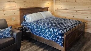 A wooden-paneled bedroom with a bed, two bedside lamps, and a chair. - Private Cabin Full Kitchen 2 (Hugo)