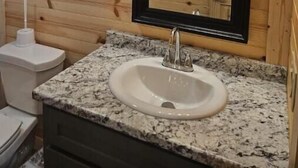 A bathroom with a granite countertop sink, a mirror with lights above it, and wooden paneling on the walls. - Private Cabin Full Kitchen 2 (Hugo)