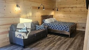 A cozy room with wooden walls, a bed with patterned bedding, a sofa with cushions, and two wall-mounted lamps. - Private Cabin Full Kitchen 2 (Hugo)