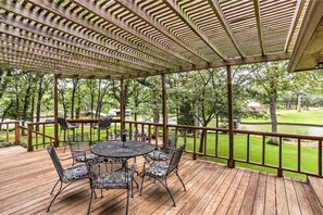 A covered outdoor deck with a round table and chairs, surrounded by a wooden railing and a view of a green landscape. - Starlight Point — Panoramic Waterfront Retreat in Star Harbor, Cedar Creek Lake (Malakoff)
