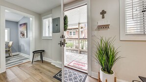 Un interior moderno con suelo de madera, una puerta que da a un balcón, una planta en maceta y un felpudo.