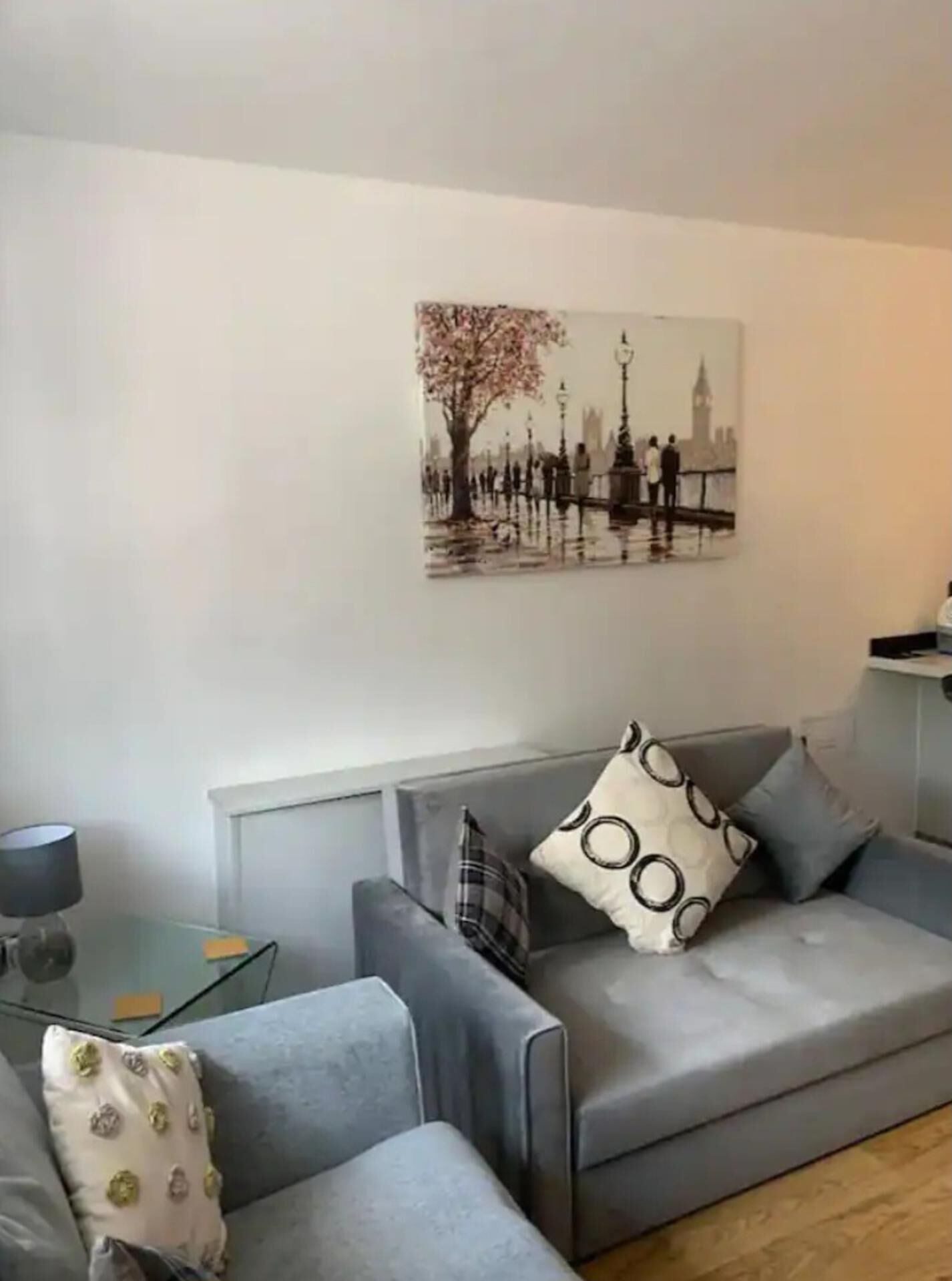 Un salon moderne avec un canapé gris, une table basse en verre et un tableau représentant un paysage urbain.