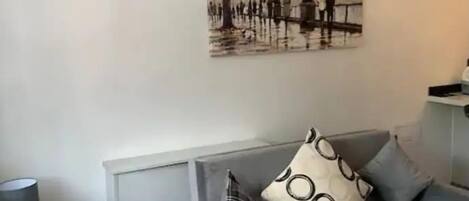 Un salon moderne avec un canapé gris, une table basse en verre et un tableau représentant un paysage urbain.