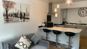 A modern kitchen with a central island, bar stools, and a hanging light fixture. - Immaculate 2-bed Apartment in Leigh (Leigh)