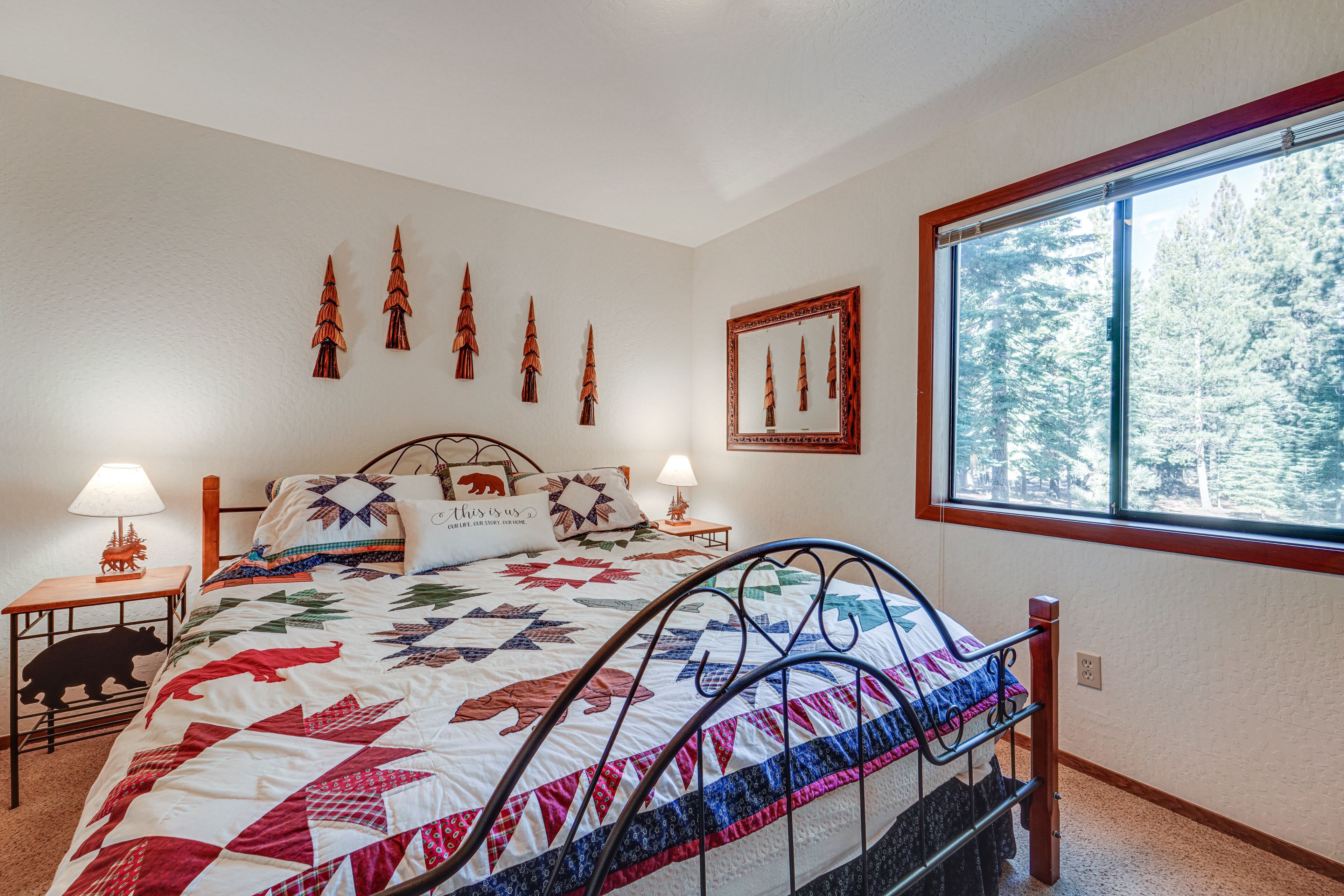 A bedroom with a large bed, two bedside tables, a nightstand, a window with a view of trees, and wall decorations.