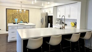 A modern kitchen with white cabinetry, a large island with bar stools, and a chandelier.