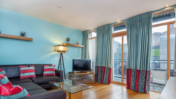 Un salon moderne avec un canapé, une table basse en verre, un téléviseur et un balcon agrémenté de rideaux à motifs.