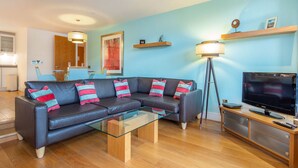 Un salon moderne avec un canapé d’angle, une table basse en verre, un téléviseur et un lampadaire.