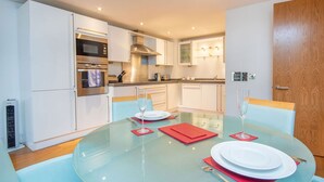 Une cuisine moderne avec des meubles blancs, des appareils en acier inoxydable et une table à manger en verre pour deux personnes.