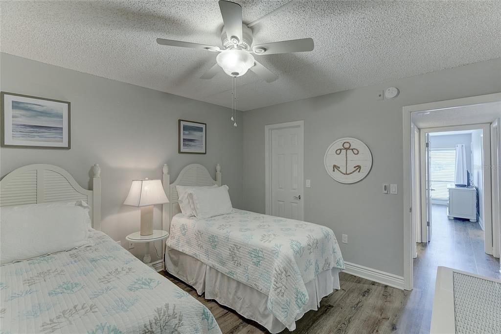 A bedroom with two beds, a ceiling fan, and a door leading to another room.