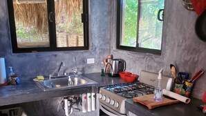 A compact kitchen with a gas stove, sink, and a small oven. There are red storage bins under the counter and a window with a view of greenery.