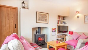 A cozy living room with a fireplace, a bookshelf, and a television. - White Cottage - UK7679 (Golspie)