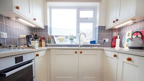 A kitchen with white cabinets, a window, a sink, and a stove. - White Cottage - UK7679 (Golspie)