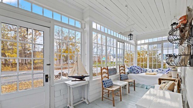 A sunlit room with large windows, wooden furniture, and a sailboat model. - Charming Coastal Biddeford Pool Home (Biddeford)