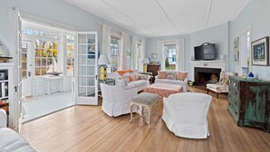 A spacious living room with a fireplace, white furniture, and a television. - Charming Coastal Biddeford Pool Home (Biddeford)