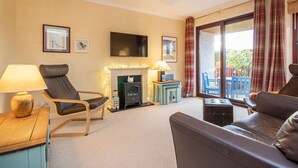 A living room with a fireplace, a flat-screen TV, a sofa, and a table with a lamp. - 2 bedroom accommodation in Dornoch (Dornoch)