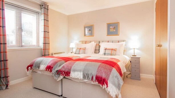 A bedroom with a bed, bedside tables, a wardrobe, and a window with curtains. - 2 bedroom accommodation in Dornoch (Dornoch)