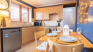 A modern kitchen with wooden cabinets, a dining table set for two, and a clock on the wall. - 2 bedroom accommodation in Dornoch (Dornoch)