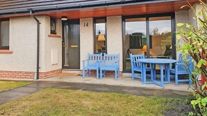 A house with a number 14 on the door, a covered porch with blue chairs and a table, and a grassy yard. - 2 bedroom accommodation in Dornoch (Dornoch)