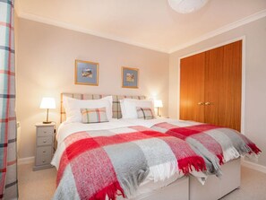 Ein Schlafzimmer mit einem Bett, zwei Nachttischlampen, einem Holzschrank und zwei gerahmten Bildern an der Wand.