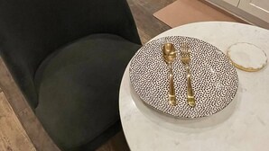 Ruokailutila, jossa on pyöreä pöytä, mustavalkoinen kuvioitu lautanen ja kultainen haarukka.