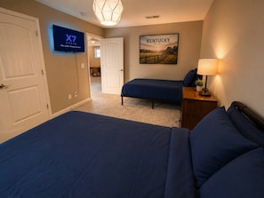 Une chambre d’hôtel avec un grand lit, un plus petit lit, une télévision, un tableau représentant un paysage du Kentucky et une lampe.