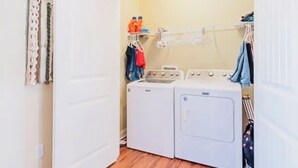 A laundry room with a white door, wooden flooring, a washing machine, a dryer, and a clothes drying rack with hanging clothes. - Modern 3BR Townhome Near Kentucky Horse Park | Georgetown, KY (Georgetown)