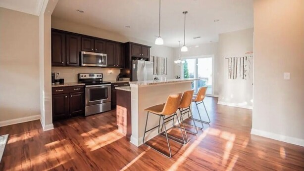 A modern kitchen with dark cabinets, stainless steel appliances, and a central island with bar stools. - Modern 3BR Townhome Near Kentucky Horse Park | Georgetown, KY (Georgetown)