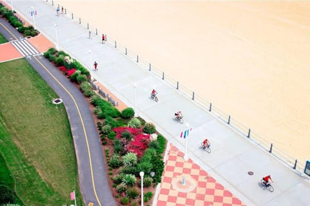 An aerial view of a pedestrian pathway with a checkered pattern, bordered by greenery and a road.
