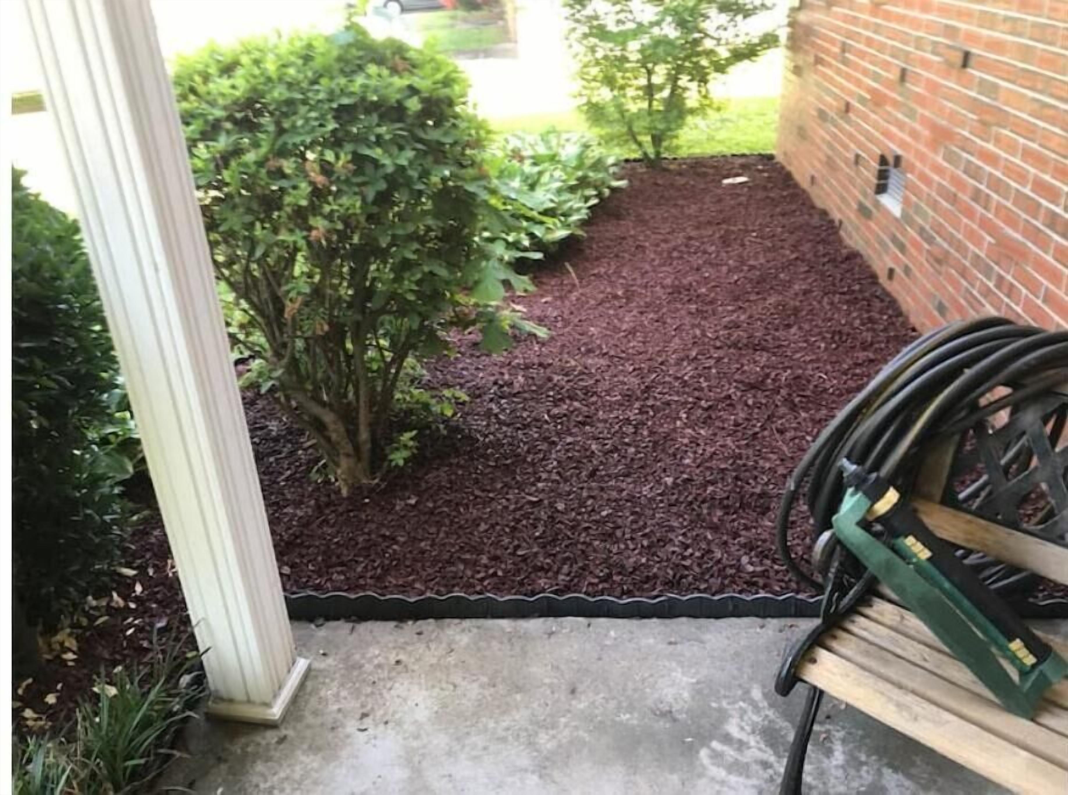 Ein Gartenbereich mit Mulch, einem kleinen Baum und einem Schlauch auf einer Bank.