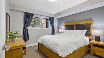 Ein ordentlich eingerichtetes Schlafzimmer mit einem großen Bett, Nachttischen, einem Fenster mit Vorhängen und einer kleinen Pflanze auf dem Nachttisch.