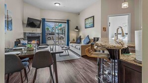 A modern living room with a fireplace, dining area, and kitchen.
