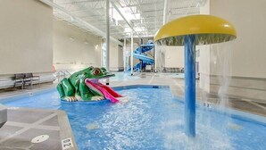 An indoor pool with a water slide and a frog-shaped play structure.