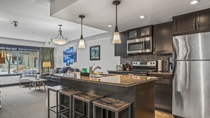 Una cocina moderna con una isla central, taburetes de bar, electrodomésticos de acero inoxidable y un amplio ventanal con vistas a la ciudad.