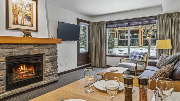 Un salón acogedor con chimenea de piedra, un ventanal con cortinas, un sofá cómodo y una mesa de comedor para dos.