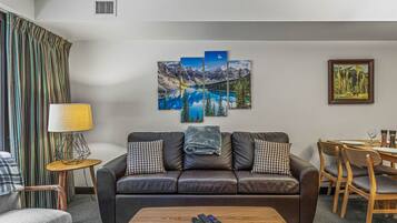 A modern living room with a leather sofa, a coffee table, a dining area with wooden chairs, and a large landscape painting on the wall.