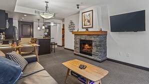 Una sala de estar moderna con chimenea de piedra, televisor de pantalla plana, comedor y cocina al fondo.