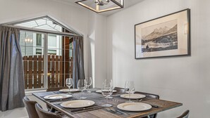 A dining area with a wooden table set for six, a large window with curtains, and a framed landscape painting on the wall. - 2 Bed |Sleeps 8|Walkout to Heated Pool|Hot Tub (Canmore)