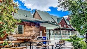 A wooden cabin with picnic tables and grills, a glass-enclosed pool, and a well-maintained lawn. - 2 Bed |Sleeps 8|Walkout to Heated Pool|Hot Tub (Canmore)