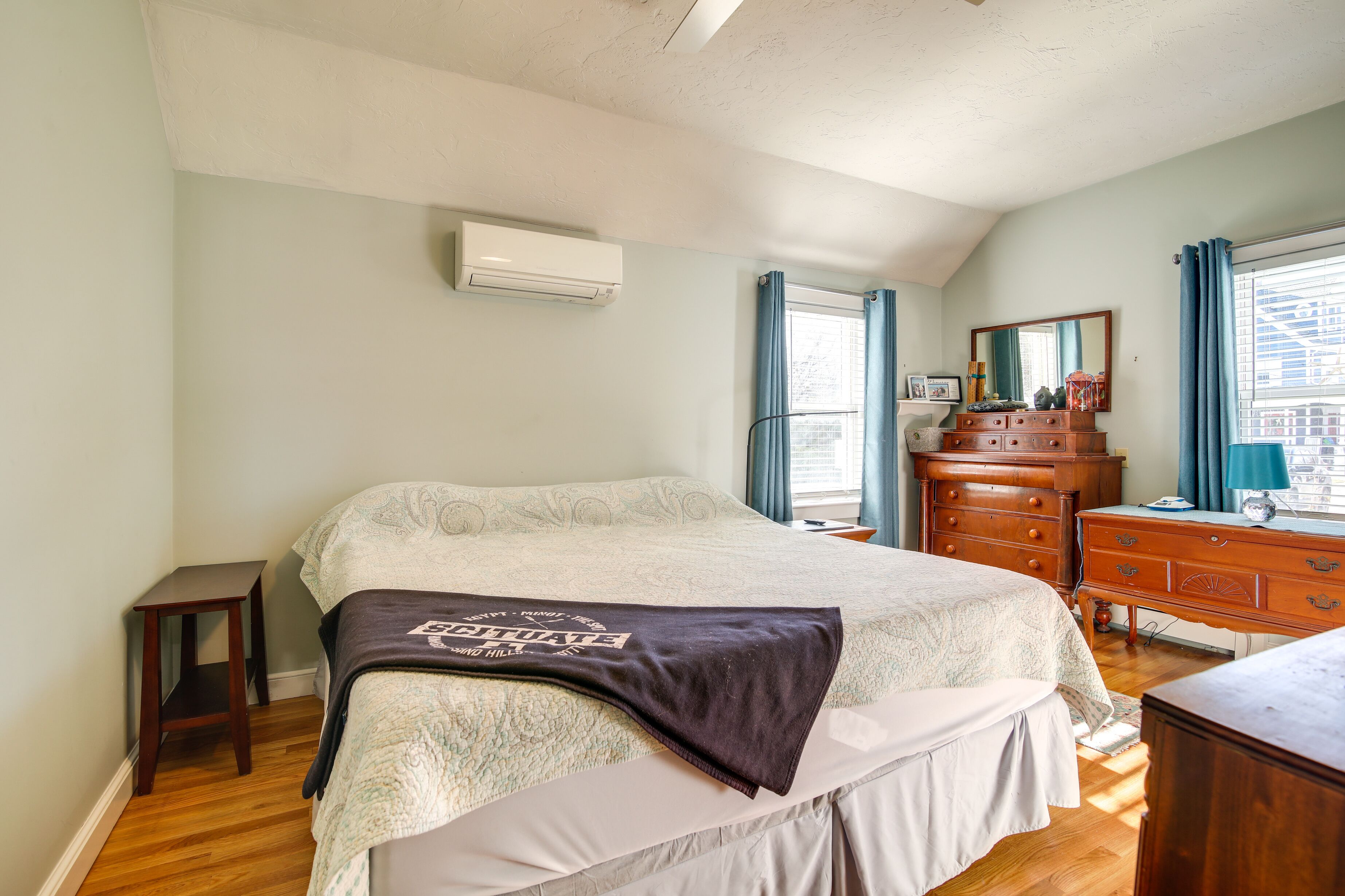 A bedroom with a bed, dresser, and a window with curtains.