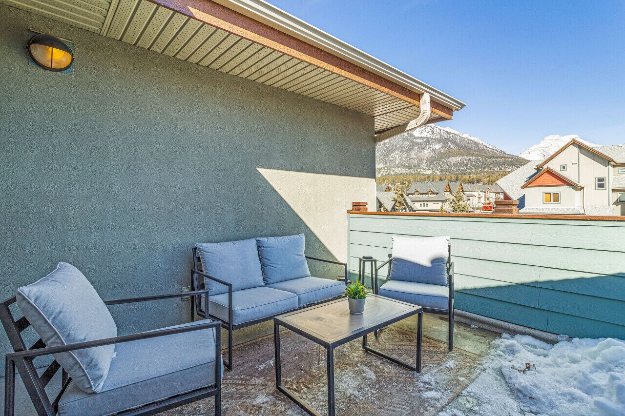 Eine Terrasse im Freien mit einer Couch, Stühlen und einem Tisch, mit Blick auf die Berge im Hintergrund.